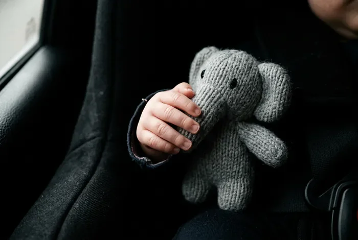 Pourquoi mon bebe pleure en voiture et comment le calmer Gros plan minimaliste de la main d'un bébé tenant un jouet dans une voiture, mise au point sur les détails.