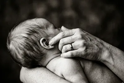 Gros plan minimaliste sur la main d'un parent touchant délicatement l'oreille d'un bébé.