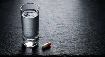 Gélule et verre d'eau sur fond sombre minimaliste