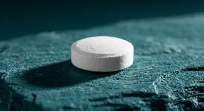 Gros plan iconique d'un comprimé blanc sur fond minéral sombre.