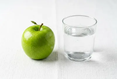 Une pomme fraîche et un verre d'eau sur fond blanc minimaliste