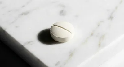 Gros plan minimaliste d'un comprimé médical sur une surface en marbre précieux.