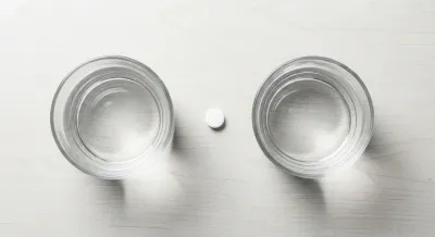 Vue minimaliste d'un comprimé et d'un verre d'eau, symbolisant la prise de lacosamide.